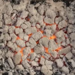 Le lit de braises d'un barbecue recouvert d'une fine cendre grise, rougeoyant faiblement, sans aucune flamme.