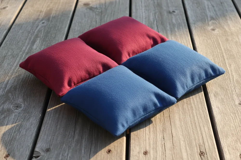 Des sacs de cornhole en tissu carrés, de deux couleurs, posés sur une surface en bois, souples et affaissés là où le remplissage se répartit.