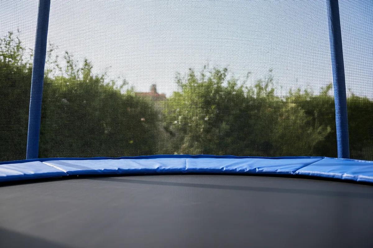 Un trampoline de jardin dont le filet de sécurité est tendu tout autour de la toile, fixé à des montants verticaux.
