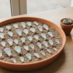 Plateau en terre cuite garni de feuilles de plantes grasses posées sur un terreau sec, certaines avec racines roses et petite rosette, à côté de trois jeunes plantes en godets